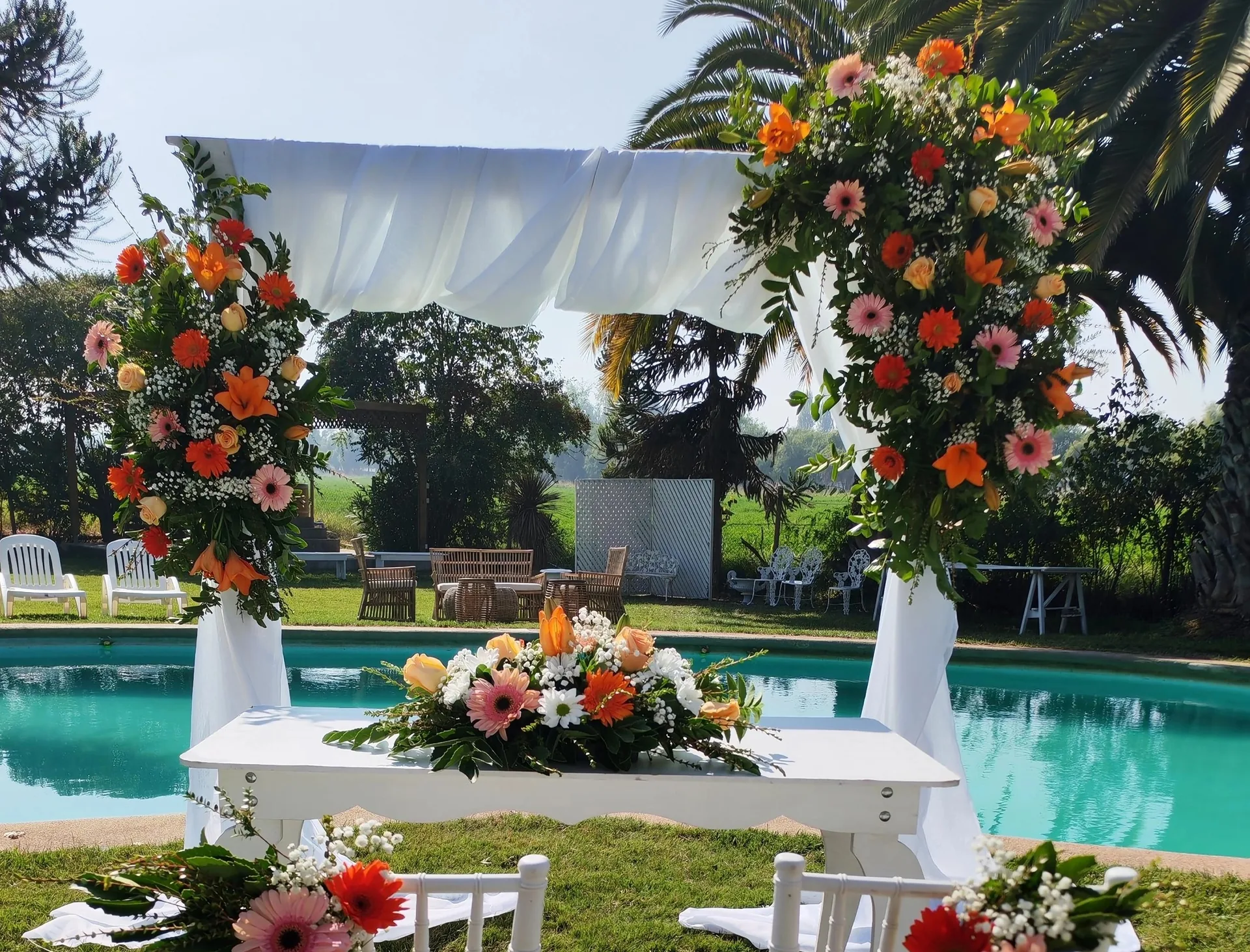 Arco floral con gerberas coral junto a una piscina con palmeras